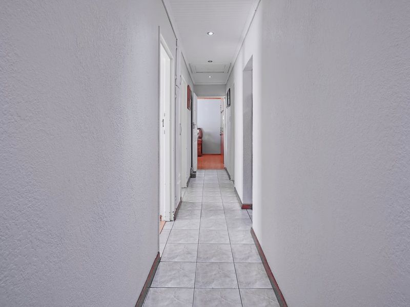A clean, neutral hallway featuring tiled flooring and recessed ceiling lighting, providing access to multiple rooms within the home.