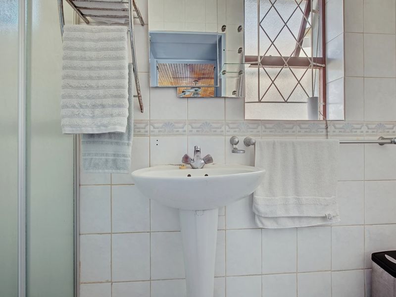 A functional bathroom featuring a pedestal basin, tiled walls, and a shower enclosure, with a window providing natural light.