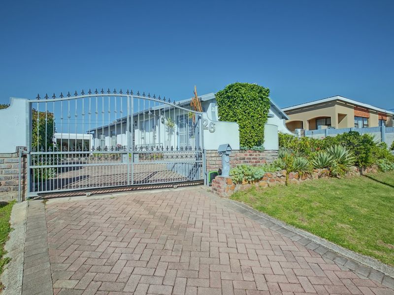 Front exterior view of the property featuring a secure metal gate, brick paved driveway, and well-maintained boundary wall with landscaped garden area.