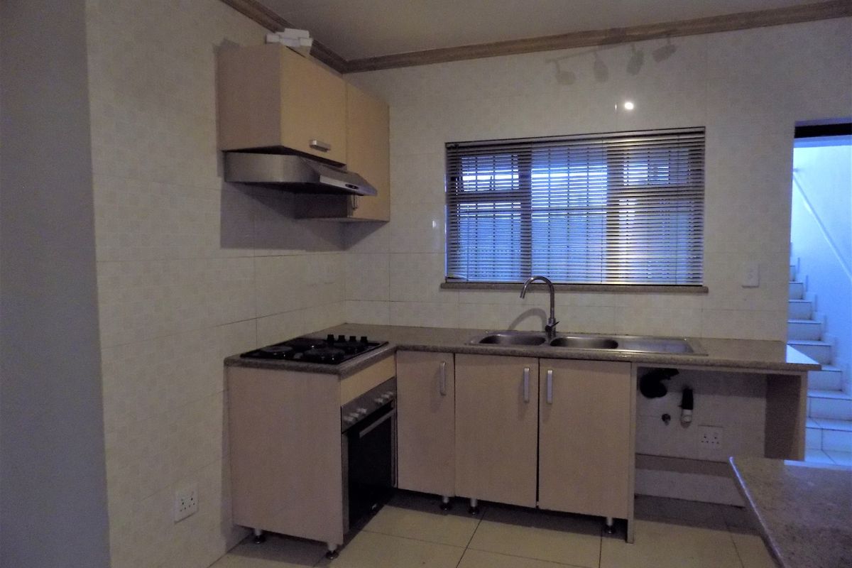 A functional kitchen featuring built-in cabinetry, a gas hob, an oven, and a stainless steel sink with tiled splashbacks and flooring.