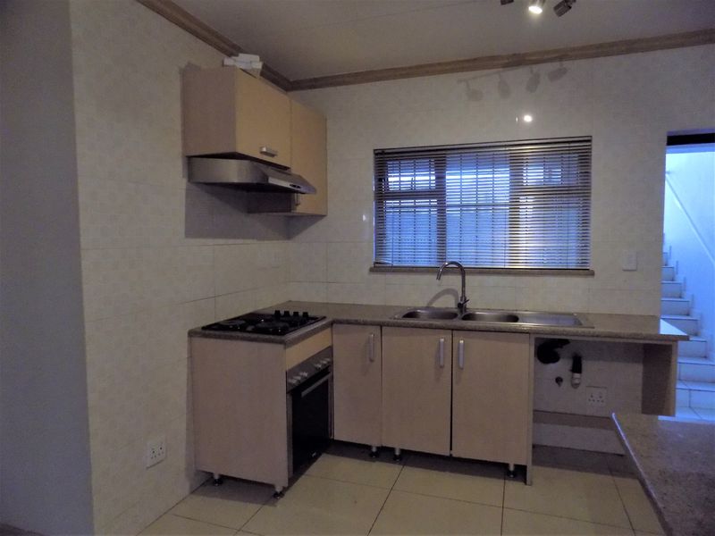 A functional kitchen featuring built-in cabinetry, a gas hob, an oven, and a stainless steel sink with tiled splashbacks and flooring.