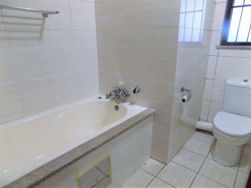 A functional bathroom featuring a built-in bathtub, standard toilet, and neutral wall and floor tiling, ready for cosmetic updates.