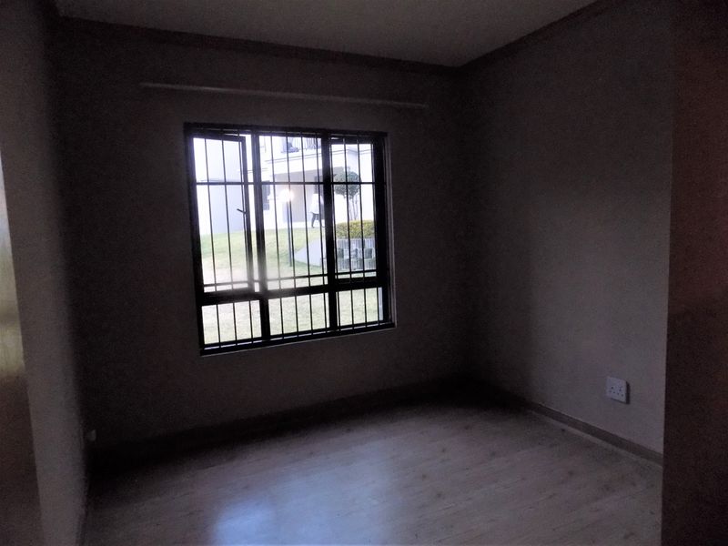 An empty bedroom featuring laminate flooring and a window fitted with security bars, providing a blank canvas for personalization.