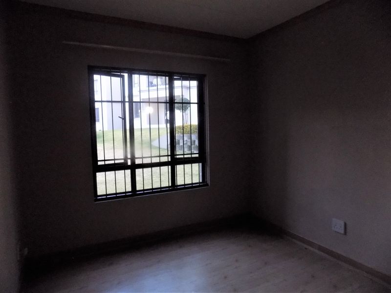 An empty bedroom featuring laminate flooring and a window fitted with security bars, offering a view of the exterior grounds.