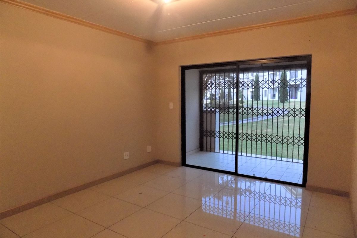 An empty living room featuring tiled flooring and a sliding glass door with a security gate leading to an outdoor area.