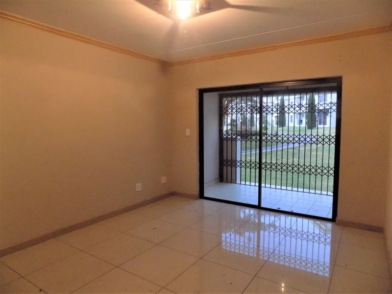 An empty living room featuring tiled flooring and a sliding glass door with a security gate leading to an outdoor area.