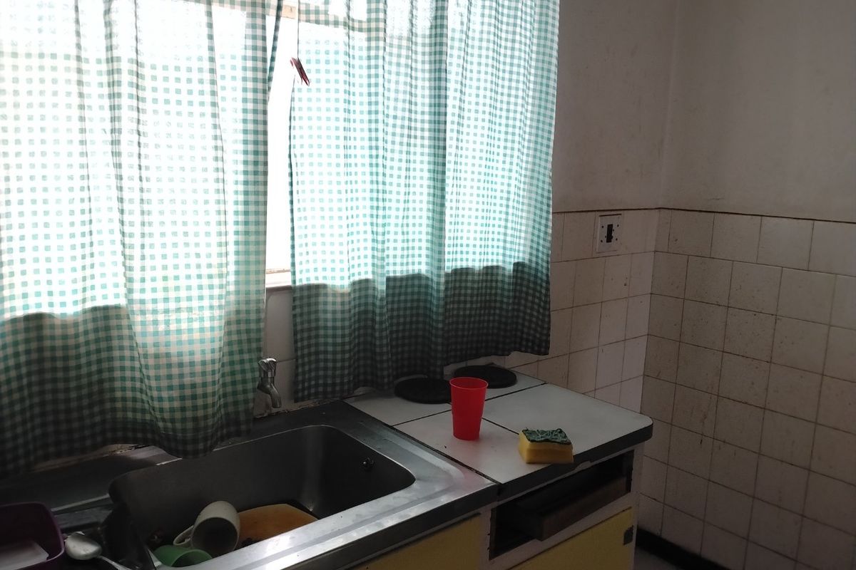 A compact kitchen area featuring a stainless steel sink, tiled splashback, and dated built-in cabinetry, offering potential for a modern renovation.
