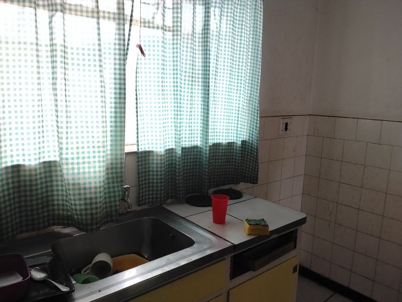 A compact kitchen area featuring a stainless steel sink, tiled splashback, and dated built-in cabinetry, offering potential for a modern renovation.