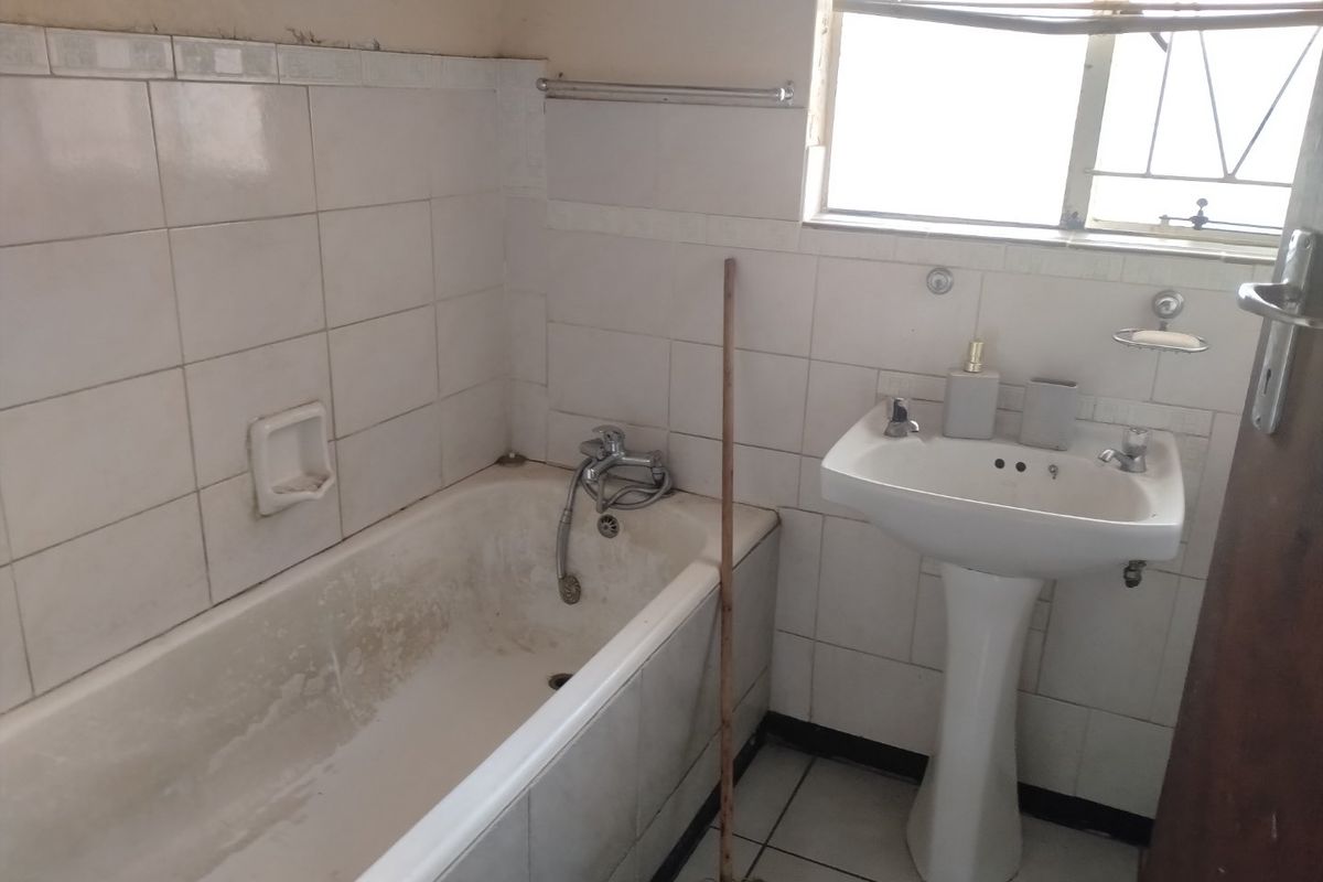 A dated bathroom featuring a pedestal basin and bathtub with wall-to-wall tiling, requiring renovation to update the finishes and fixtures.
