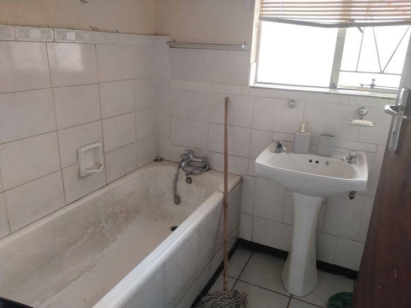 A dated bathroom featuring a pedestal basin and bathtub with wall-to-wall tiling, requiring renovation to update the finishes and fixtures.