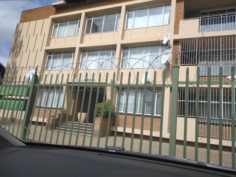Front elevation of the Villa Rosa apartment complex, featuring brick facade, security fencing with razor wire, and multiple satellite dish installations.