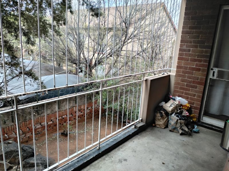A balcony area featuring a concrete floor, brick wall, and metal security railing overlooking a garden space.