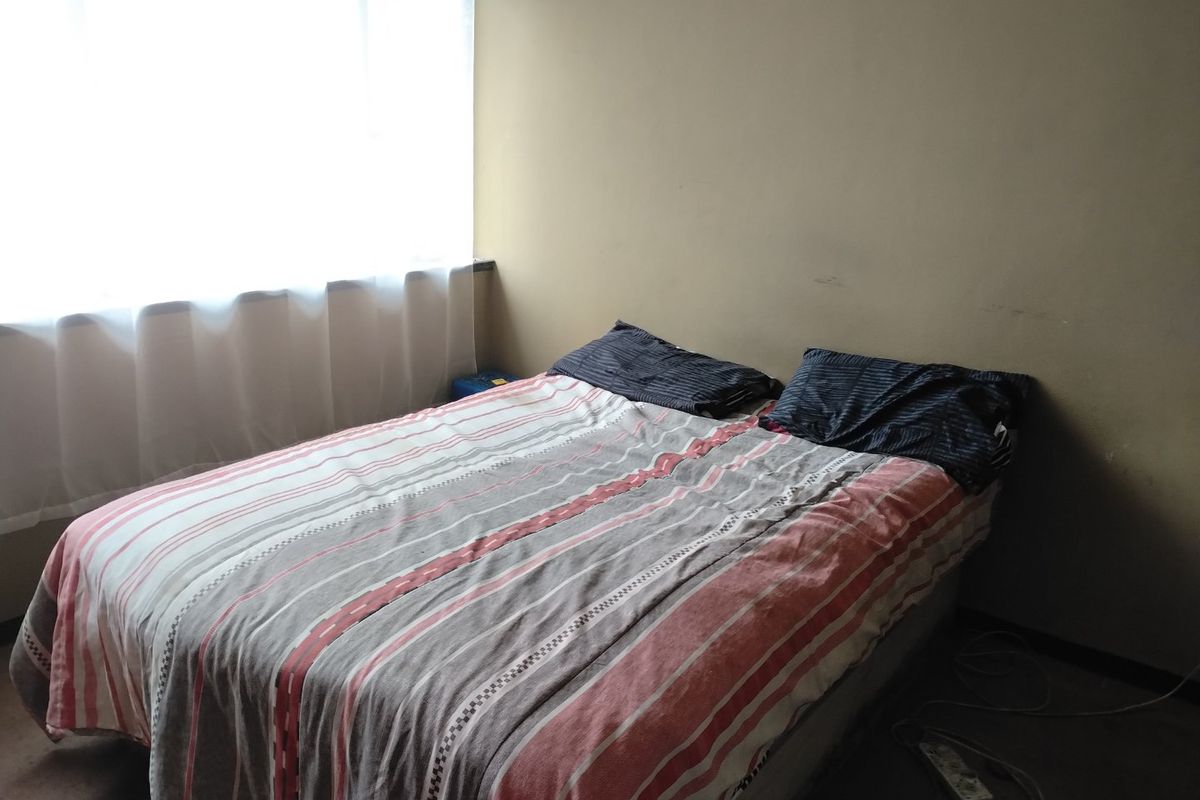 A bedroom featuring a large window with natural light, requiring cosmetic updates to the wall finishes and flooring.