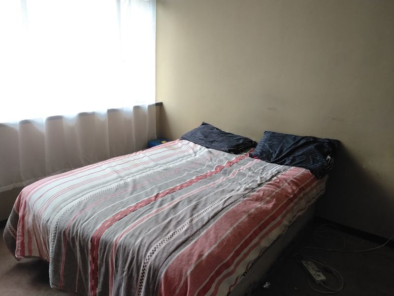 A bedroom featuring a large window with natural light, requiring cosmetic updates to the wall finishes and flooring.