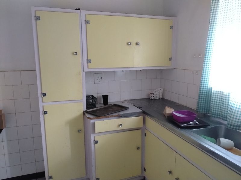 A dated kitchen featuring original yellow cabinetry, a stainless steel sink, and a tiled backsplash, offering potential for a modern renovation.