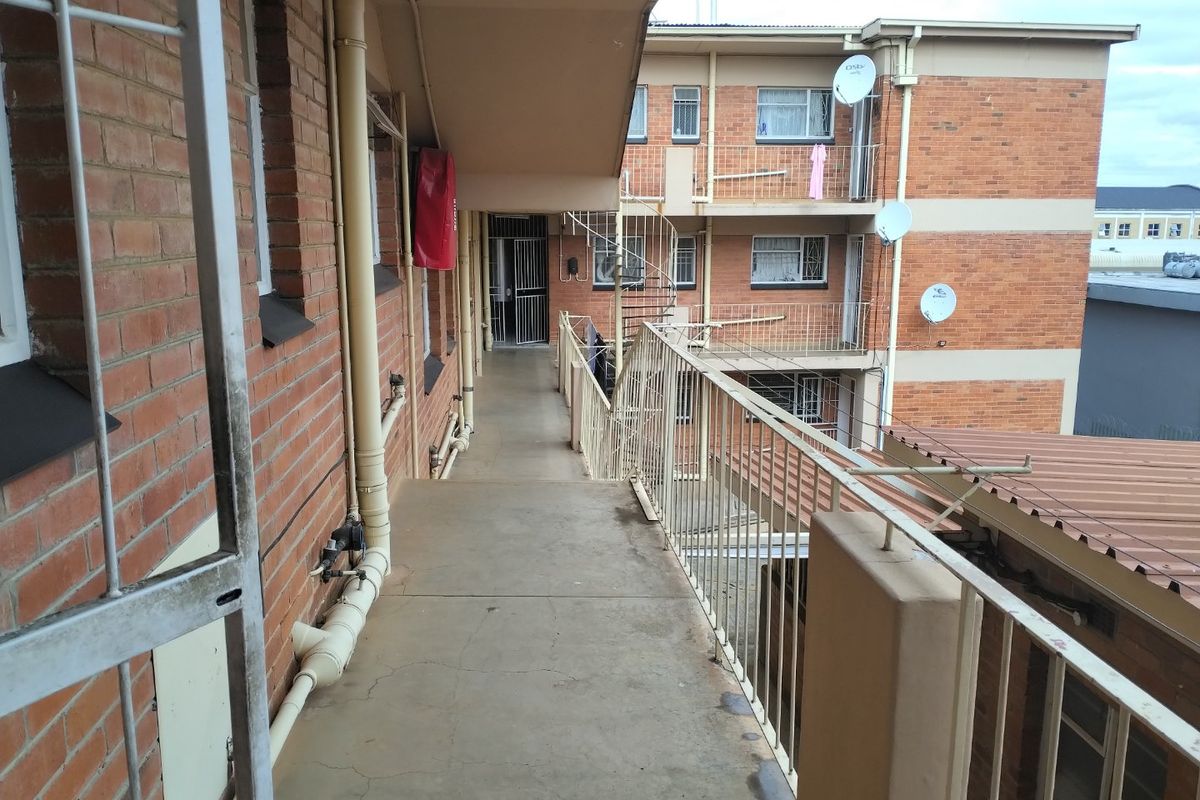 Exterior walkway of an apartment complex featuring brick facade, metal balustrades, and a spiral staircase providing access to upper levels.