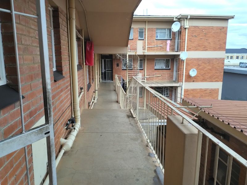 Exterior walkway of an apartment complex featuring brick facade, metal balustrades, and a spiral staircase providing access to upper levels.