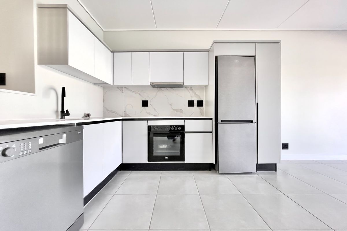 Modern, minimalist kitchen featuring white cabinetry, marble-look splashback, integrated oven, extractor fan, and sleek stainless steel appliances with neutral floor tiling.