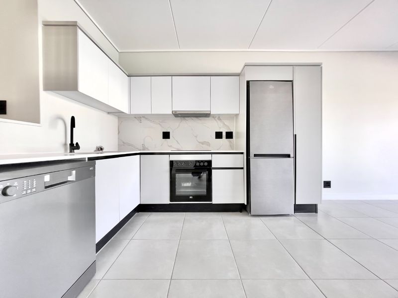 Modern, minimalist kitchen featuring white cabinetry, marble-look splashback, integrated oven, extractor fan, and sleek stainless steel appliances with neutral floor tiling.