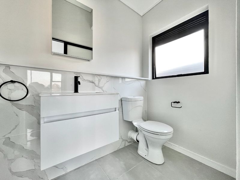 Modern bathroom featuring a wall-mounted vanity, marble-look tiled splashback, black fixtures, and a clean, contemporary aesthetic.