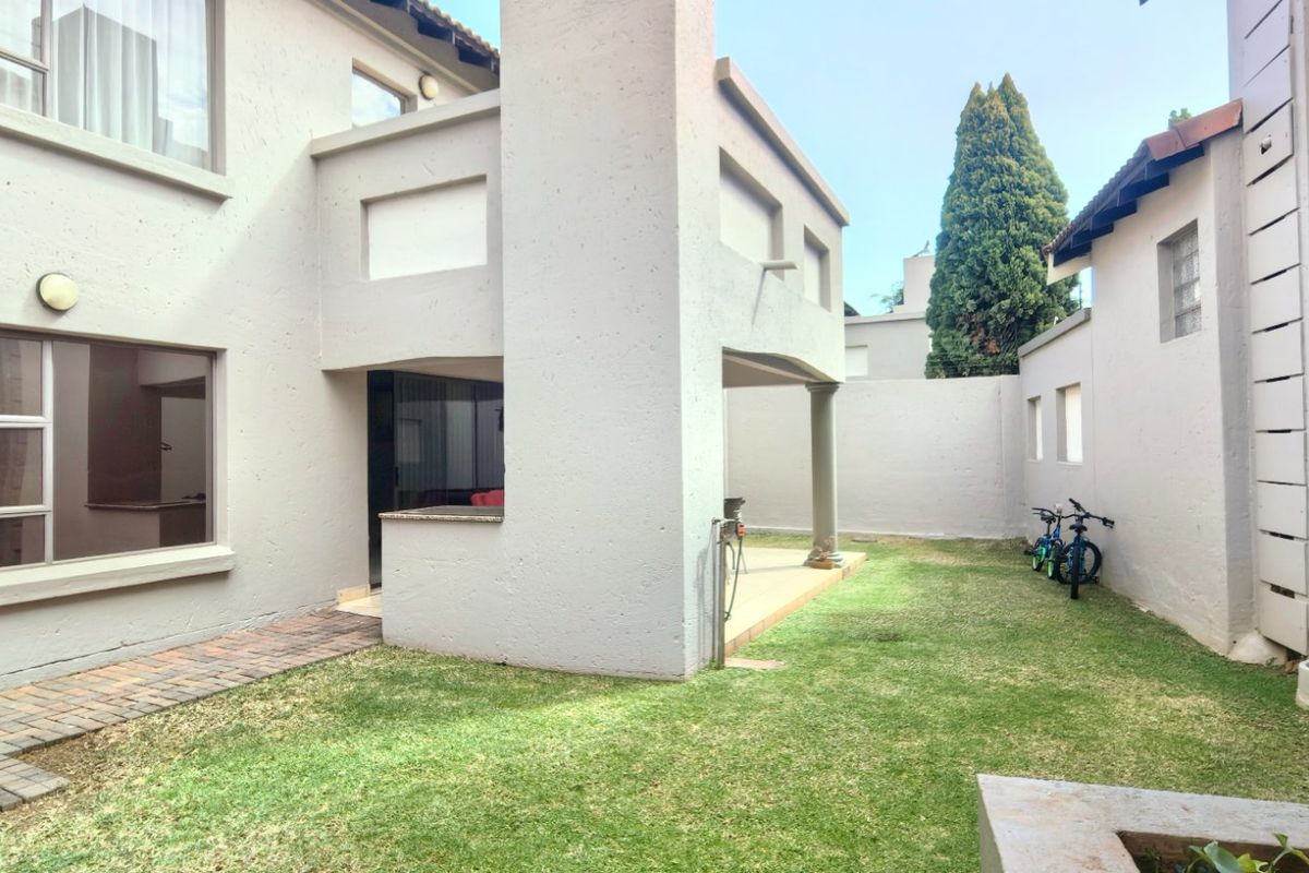 A private rear garden featuring a paved walkway, a covered patio area, and a well-maintained lawn enclosed by boundary walls.