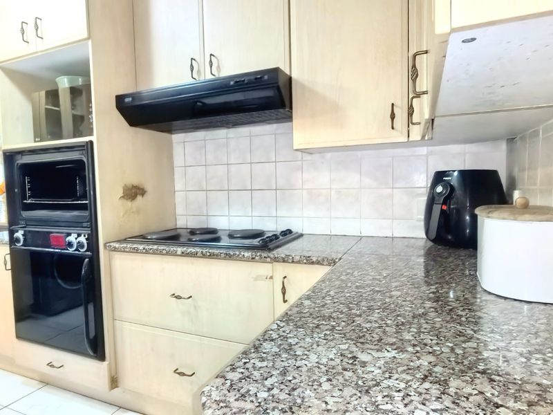 Functional kitchen featuring granite countertops, built-in oven, electric hob, extractor fan, and tiled backsplash with ample cabinetry for storage.