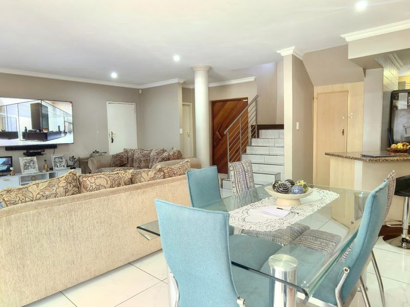 Spacious open-plan living and dining area featuring tiled floors, a breakfast bar with granite countertops, and a staircase leading to the upper level.
