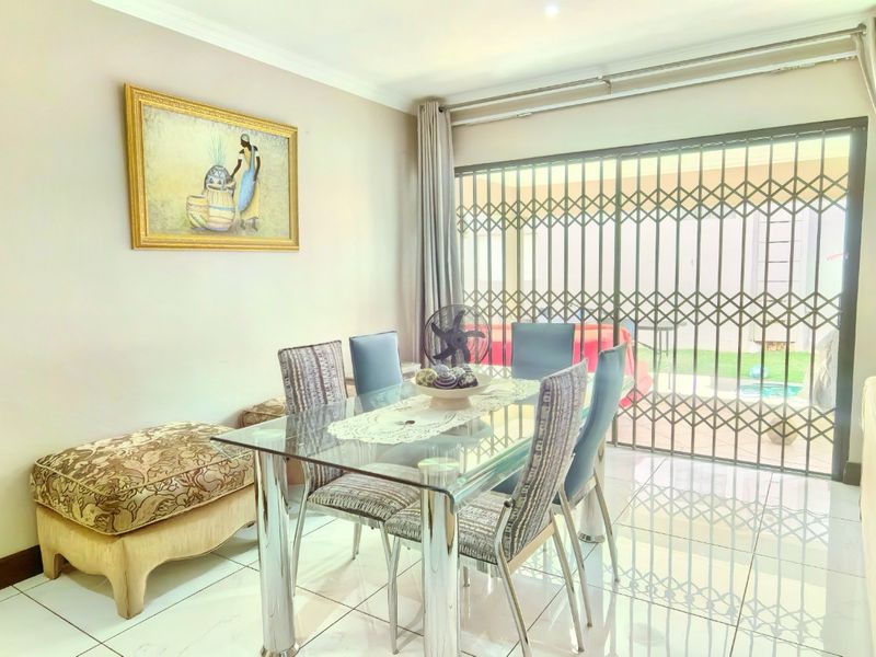 A bright dining area featuring tiled flooring and a sliding glass door with a security gate, providing direct access to the outdoor patio area.
