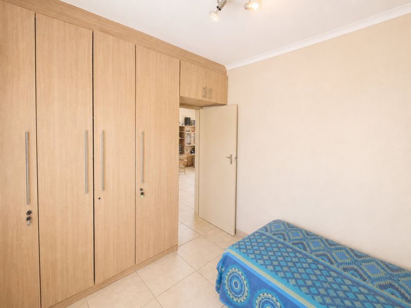 A bedroom featuring light wood-finish built-in cupboards, neutral tiled flooring, and a doorway leading to an adjacent living space.