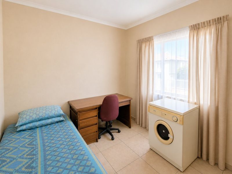A functional bedroom featuring tiled flooring, neutral wall finishes, and a window with installed curtain tracks.