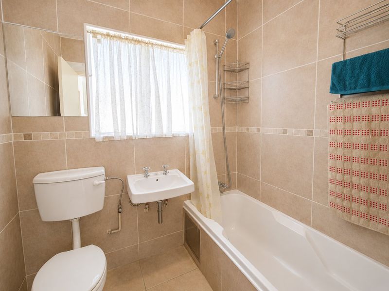 A functional bathroom featuring neutral ceramic wall and floor tiles, a wall-mounted basin, a close-coupled toilet, and a bathtub with a shower mixer.
