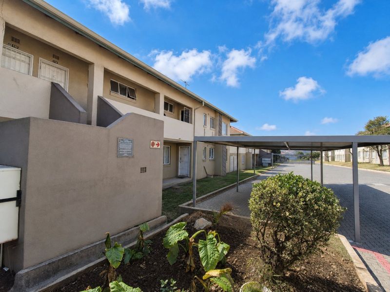 Exterior view of an apartment complex featuring a covered carport, paved driveway, and building facade with security gates.