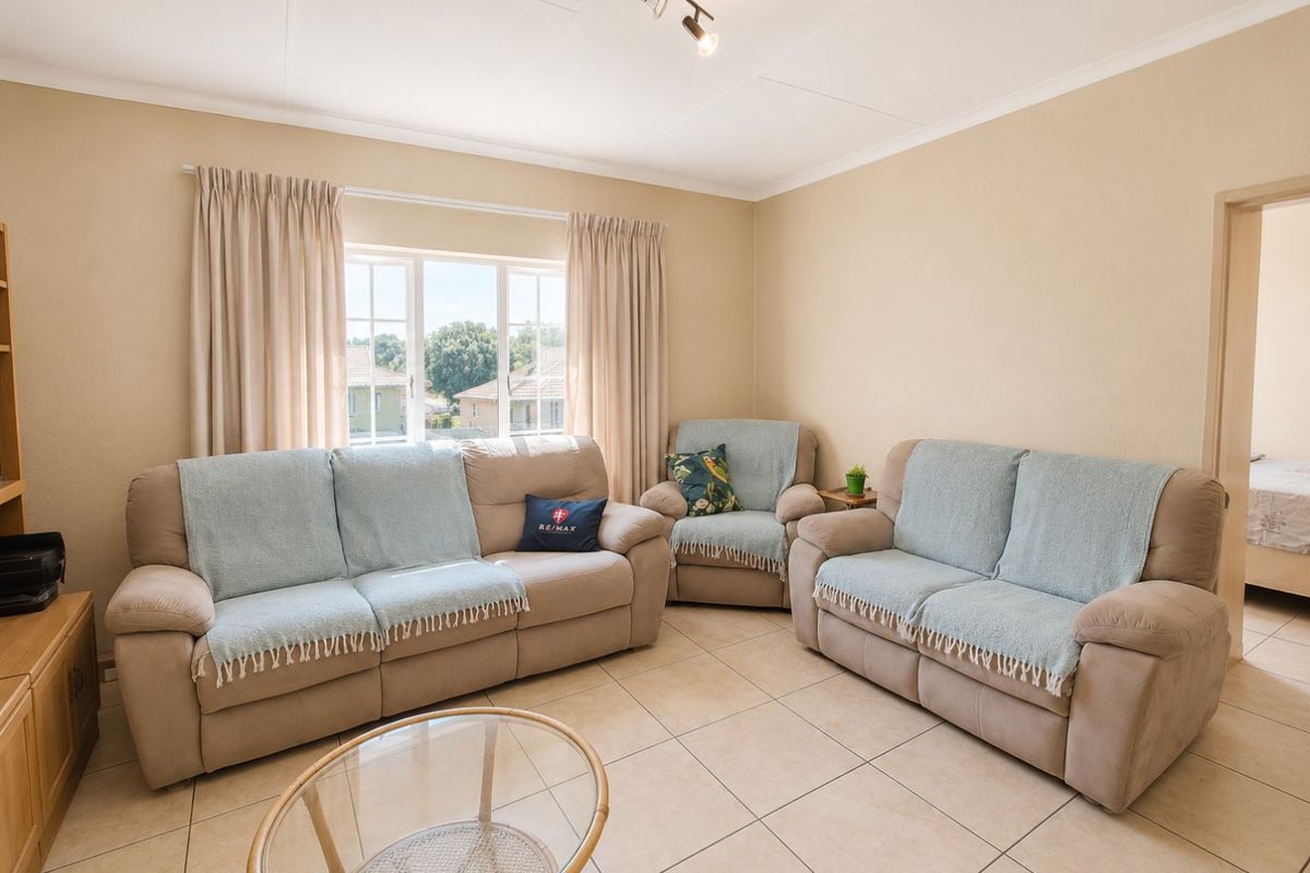 A well-lit living room featuring neutral tiled flooring, track lighting, and a large window with curtain rails, offering a comfortable and functional living space.