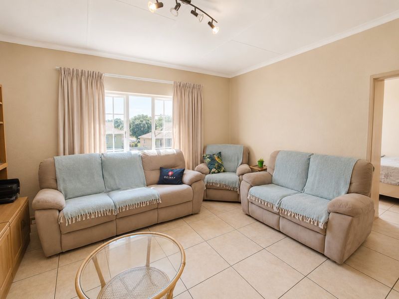 A well-lit living room featuring neutral tiled flooring, track lighting, and a large window with curtain rails, offering a comfortable and functional living space.