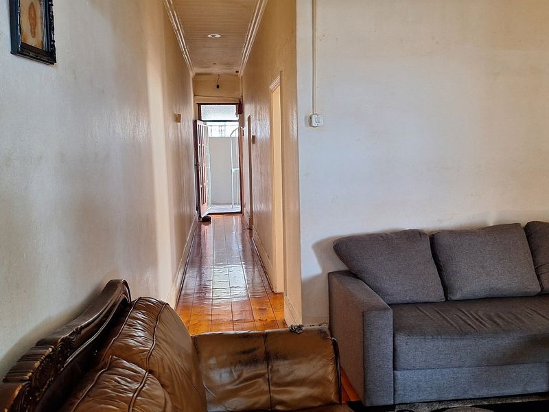 A long hallway featuring polished hardwood flooring and coved ceilings, leading towards an exterior doorway, showing signs of wear on the wall surfaces.