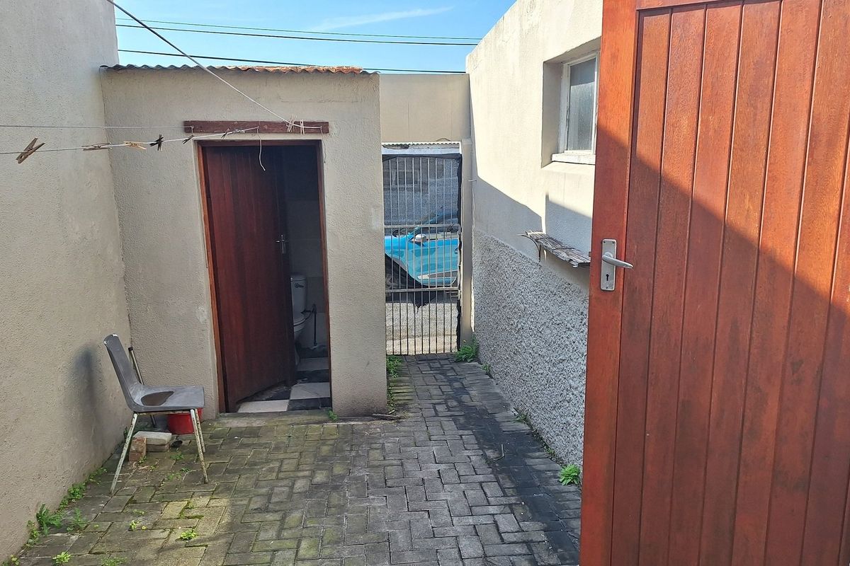 A rear courtyard area featuring paved flooring, a metal security gate, and access to an external toilet facility.