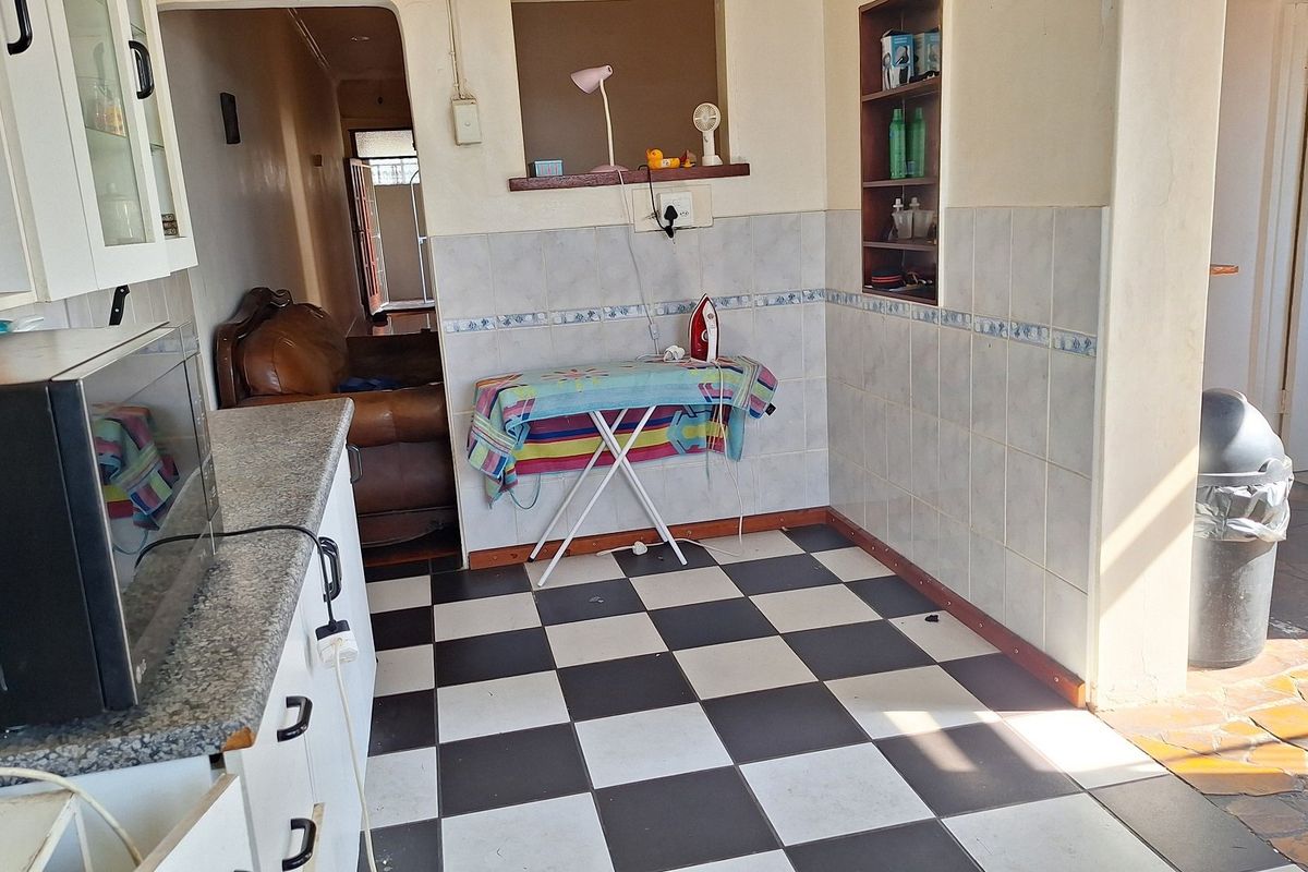 A functional kitchen area featuring checkered floor tiles, granite countertops, and built-in wall shelving, offering potential for a modern renovation.