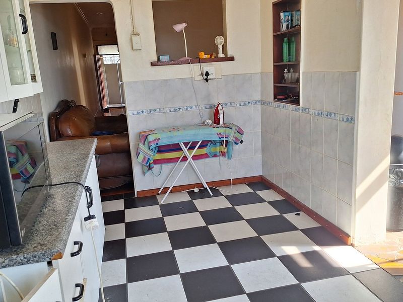 A functional kitchen area featuring checkered floor tiles, granite countertops, and built-in wall shelving, offering potential for a modern renovation.