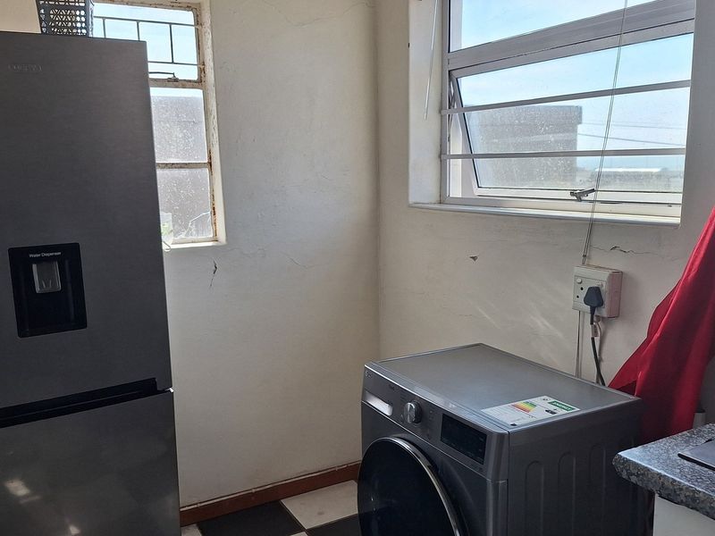 A functional laundry area featuring a sink, countertop space, and dedicated plumbing connections for appliances, with windows providing natural light.