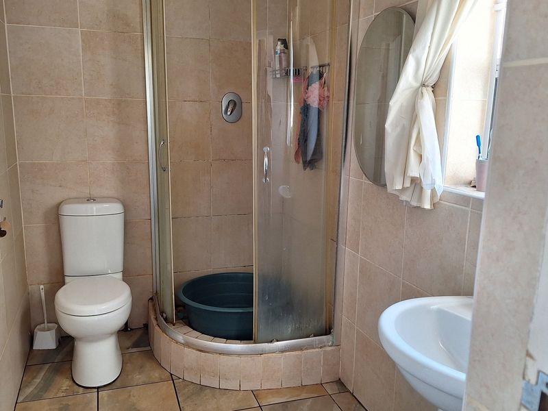 A compact bathroom featuring a corner shower enclosure, pedestal basin, and toilet with neutral wall and floor tiling.