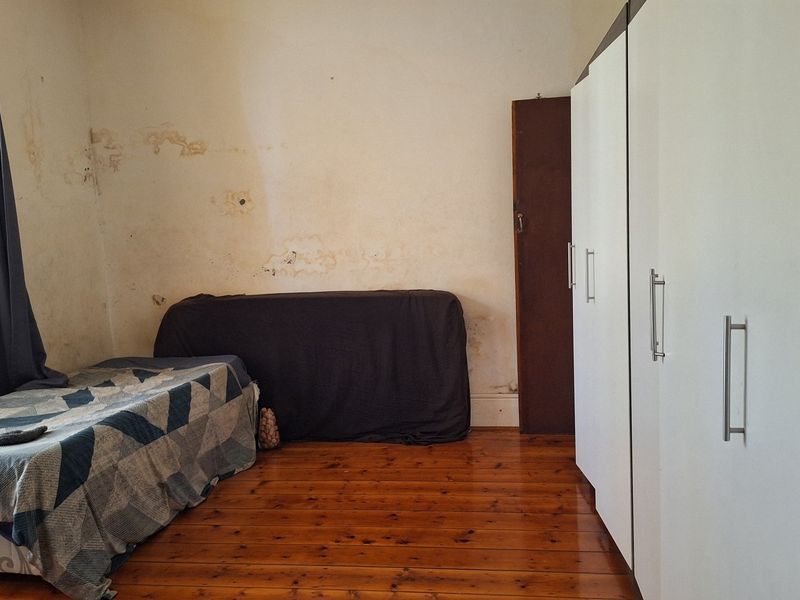 Bedroom featuring timber flooring and built-in cupboards, requiring wall repairs and cosmetic updates to restore the space.