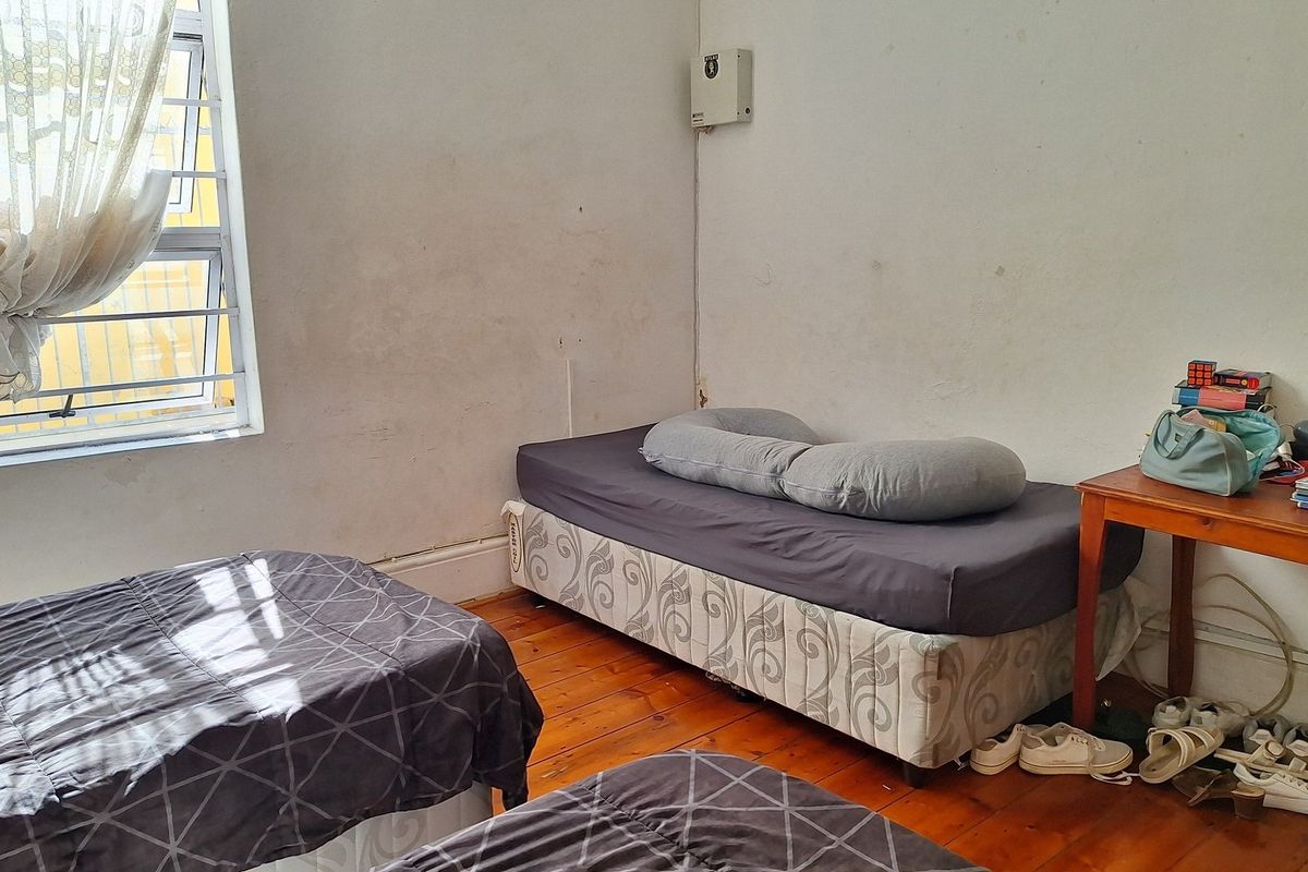 A bedroom featuring timber flooring, security bars on the window, and an exposed electrical distribution board on the wall.