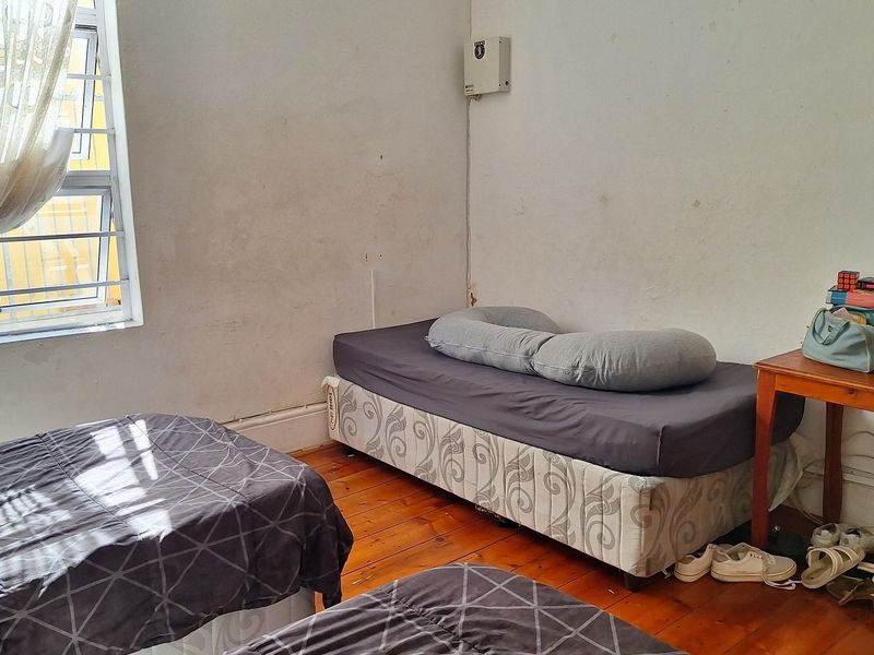 A bedroom featuring timber flooring, security bars on the window, and an exposed electrical distribution board on the wall.
