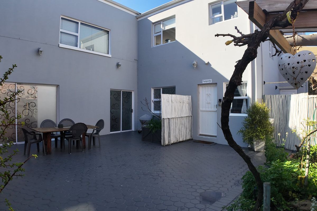 A paved rear courtyard featuring a timber pergola, sliding door access, and exterior wall lighting, providing a functional outdoor entertainment space.