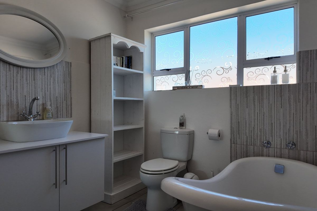A well-maintained bathroom featuring a modern vessel sink, vanity cabinet, toilet, and a freestanding bathtub with decorative frosted window glass.