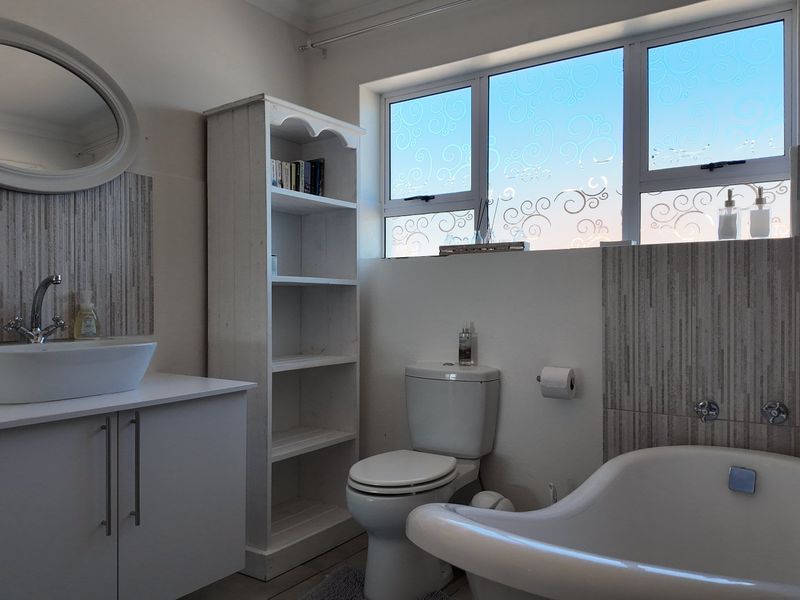 A well-maintained bathroom featuring a modern vessel sink, vanity cabinet, toilet, and a freestanding bathtub with decorative frosted window glass.
