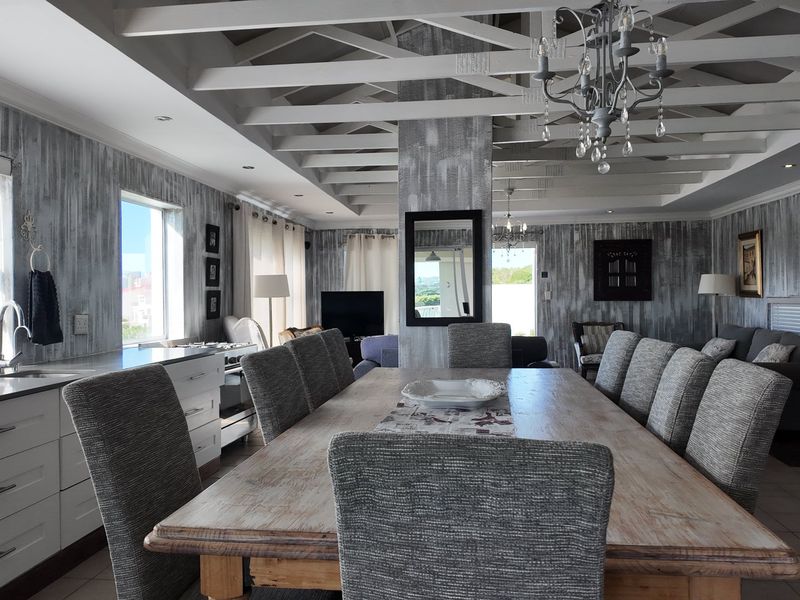 Spacious open-plan living and dining area featuring exposed timber ceiling beams, modern kitchen cabinetry, and large windows providing ample natural light.