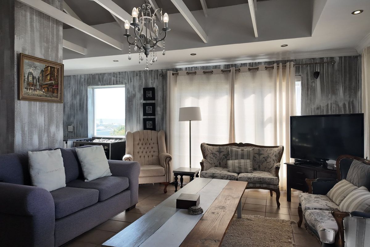 Spacious living room featuring exposed ceiling beams, a decorative chandelier, tiled flooring, and large windows providing ample natural light.