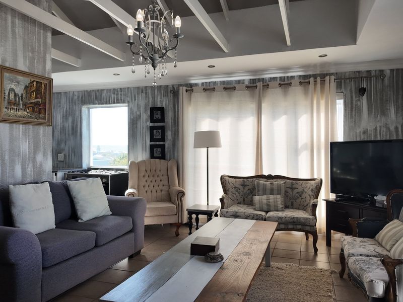 Spacious living room featuring exposed ceiling beams, a decorative chandelier, tiled flooring, and large windows providing ample natural light.