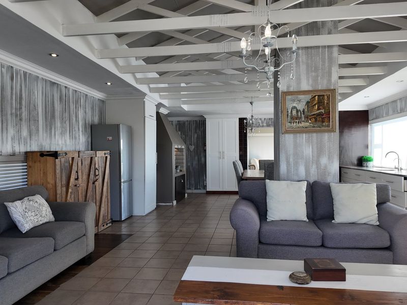 Spacious open-plan living area featuring exposed white timber ceiling beams, tiled flooring, a built-in fireplace, and a modern kitchen with integrated appliances.